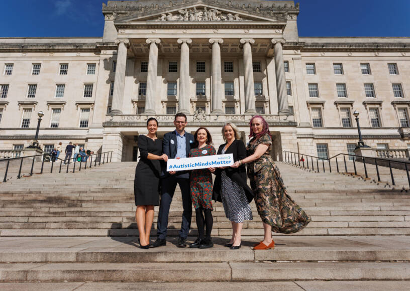 A group of people stand outside Stormont building holding a sign that reads '#AutisticMindsMatter'