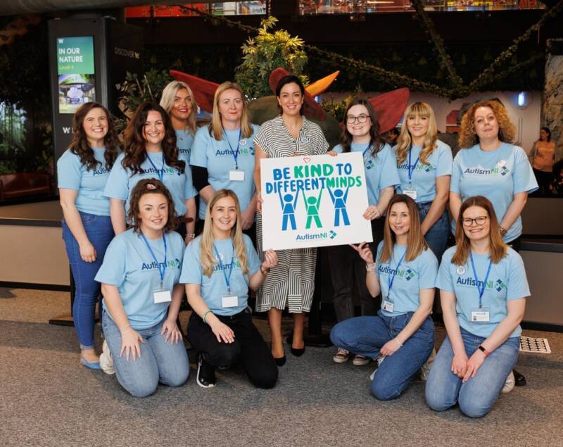 Autism NI staff members posing and smiling while holding a 'be kind to different minds' poster
