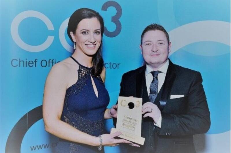 Two people smile and pose together with an award