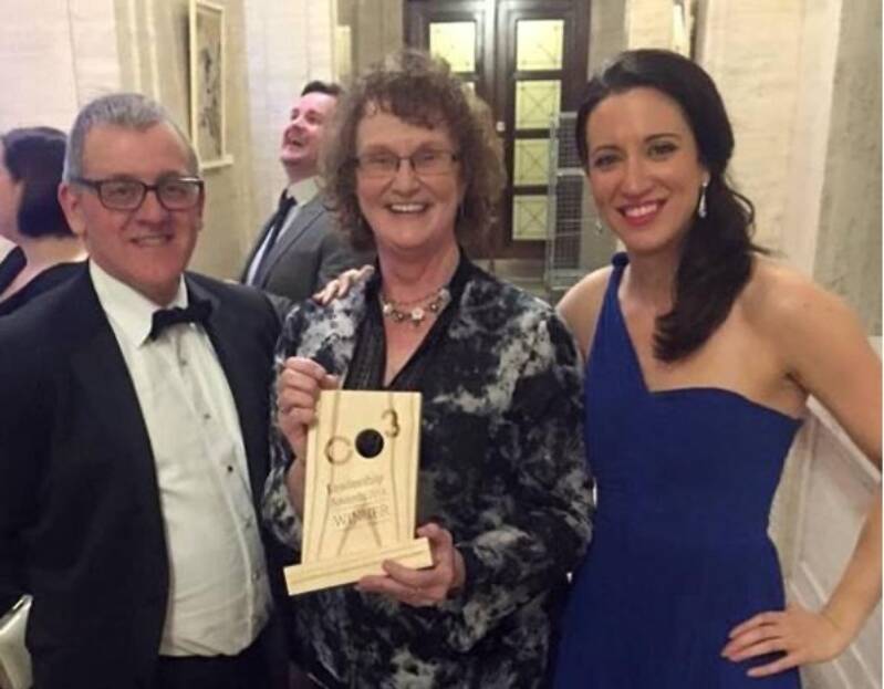 Several people smile and pose together with an award