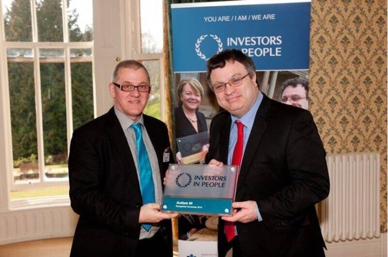 Two men in suits smile and pose with an award