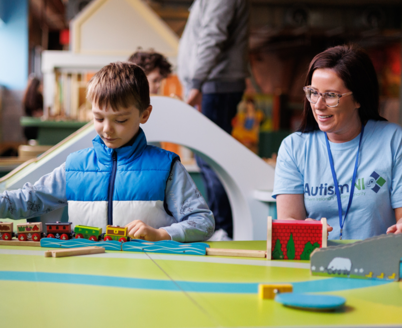 Autism NI member pictured beside a small child playing with toy trains