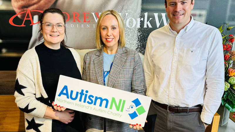 Several people pose together and hold an Autism NI sign
