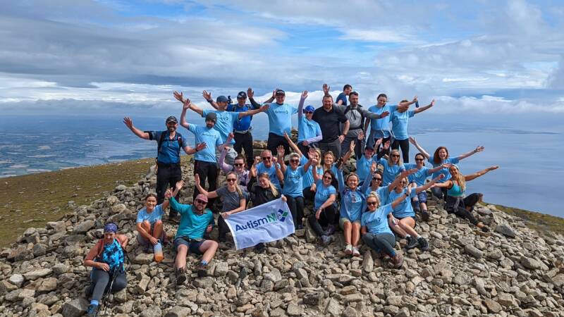 A group of people pose with their arms raised on top of a mountain