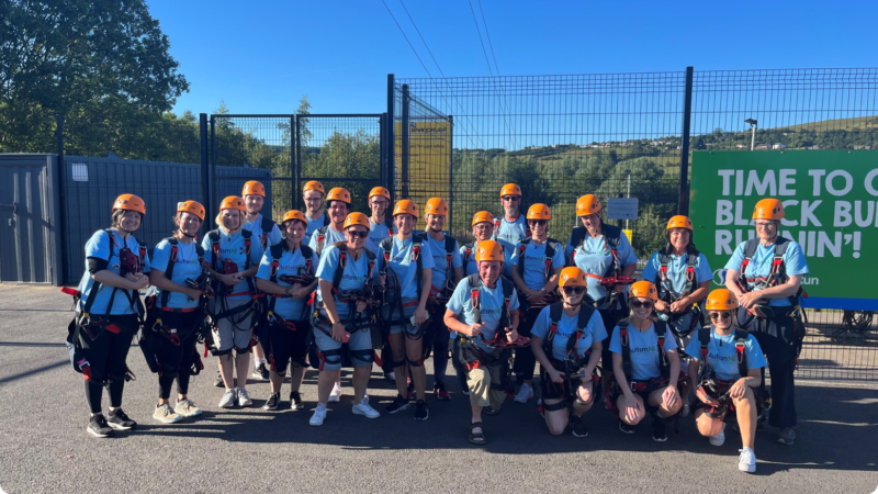 A group of people pose together wearing Autism NI T-shirts and helmets