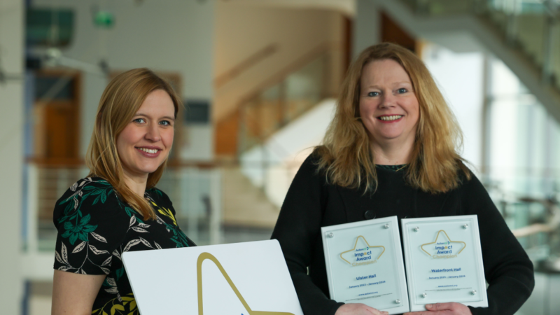 Two women smiling and holding impact award plaques