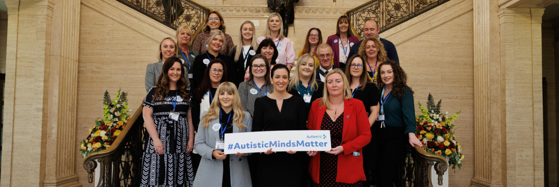 A group of people standing and posing on a staircase holding a sign that reads '#AutisticMindsMatter'