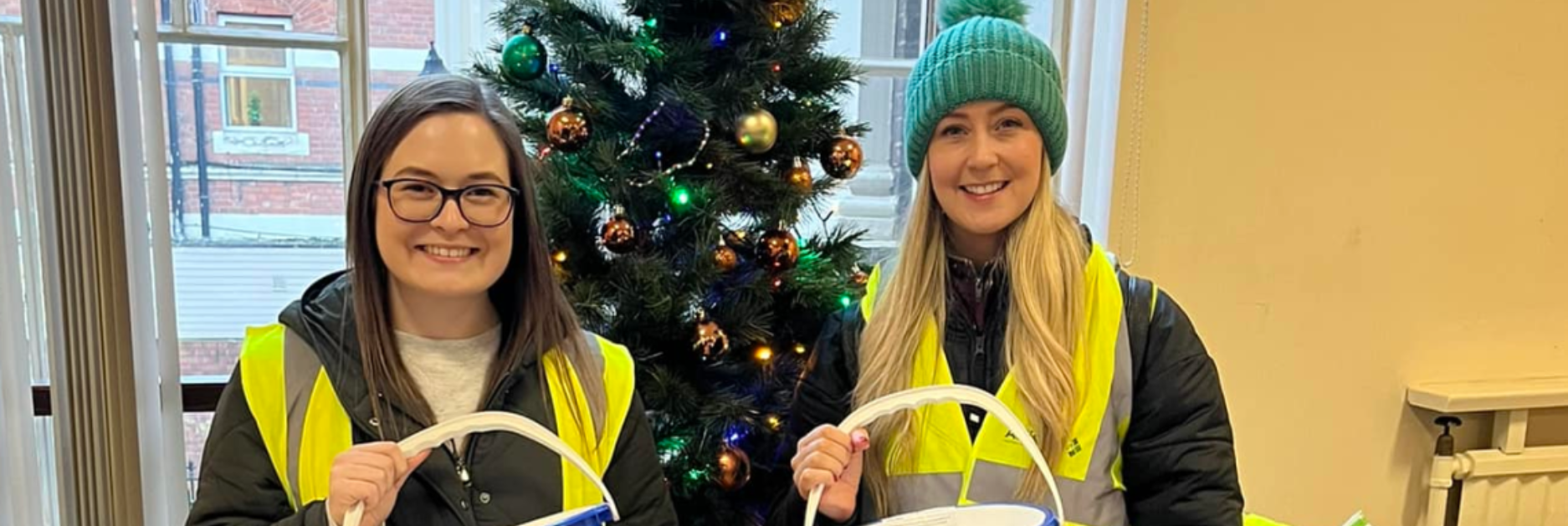 Autism NI volunteers wearing high-vis jackets and holding collection buckets in front of a Christmas tree