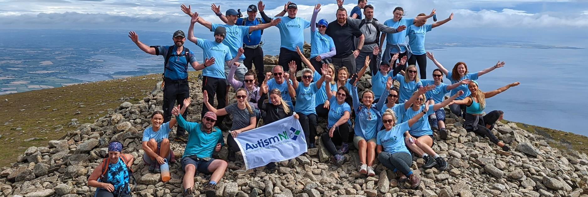 A group of people pose with their arms raised on top of a mountain