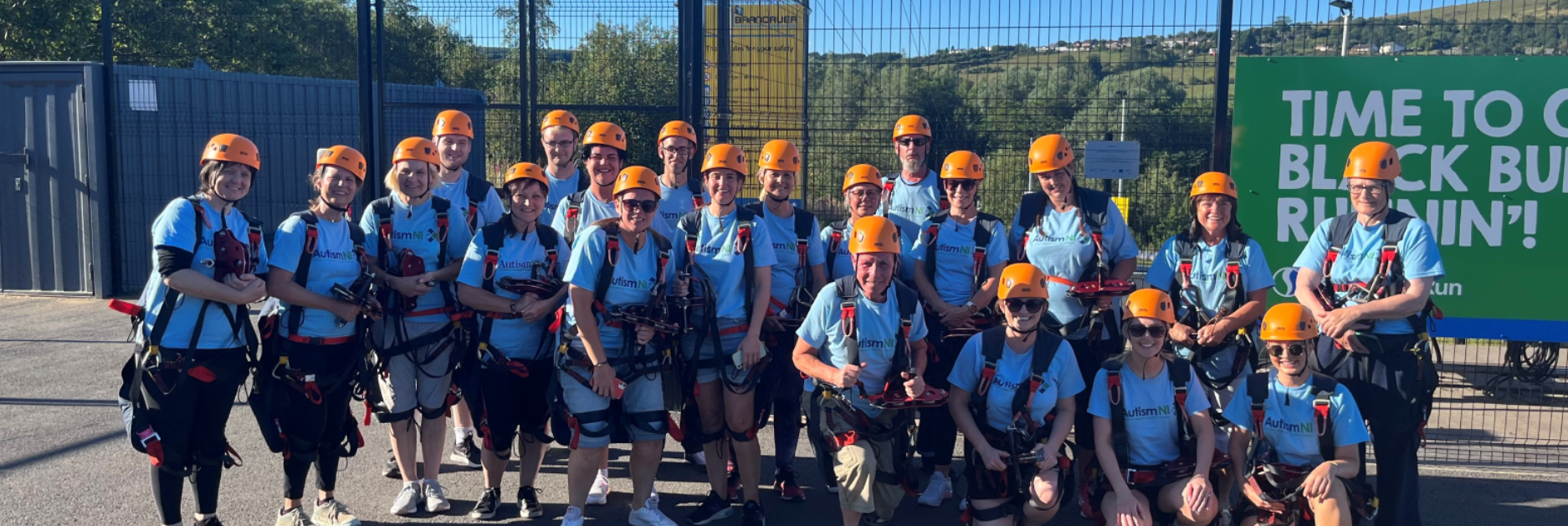 A group of people pose together wearing Autism NI T-shirts and helmets
