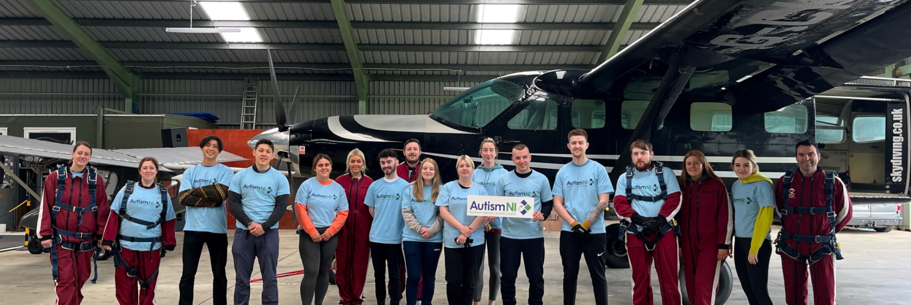 A group of people in Autism NI T-shirts standing in front of a small aircraft