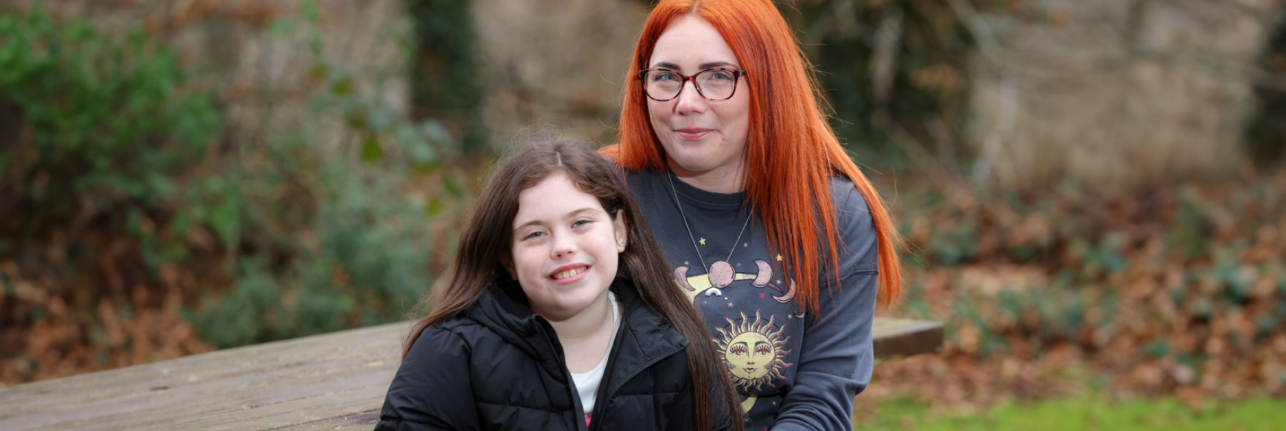 A woman and her child smiling and sitting at a picnic bench