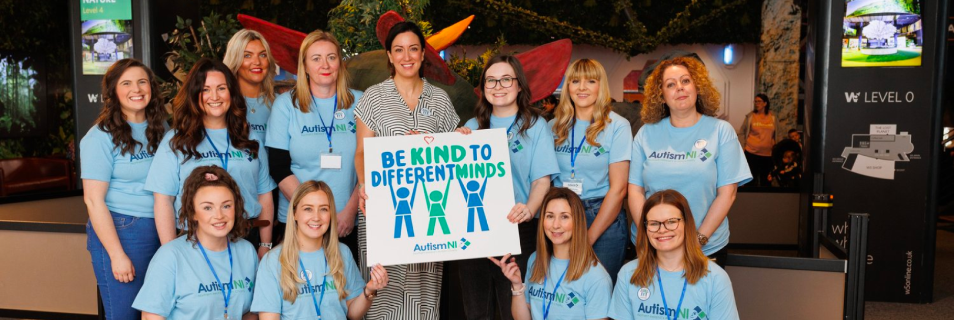 Autism NI staff members pose and smile for a photo while holding a 'Be kind to different minds' poster