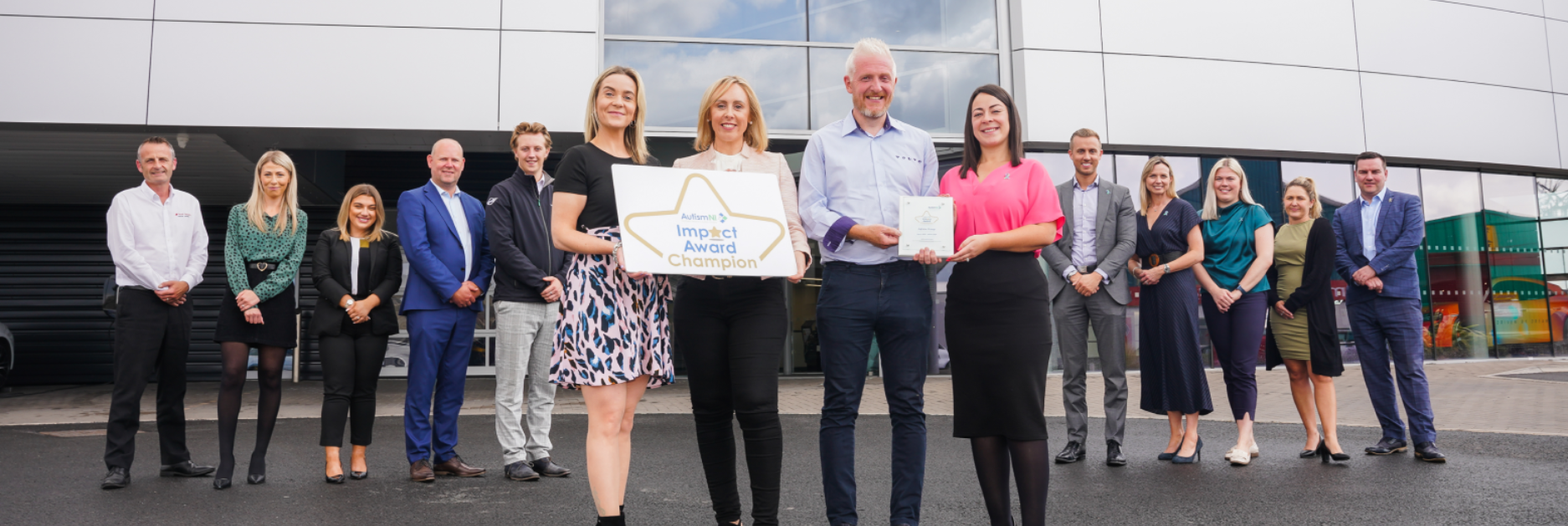 A group of people standing outside a building, holding sign that reads 'impact award champion'