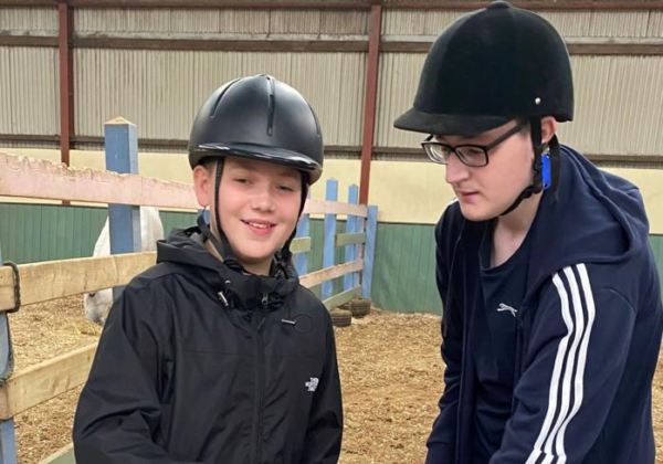 Two boys pictured wearing helmets and brushing a pony's back