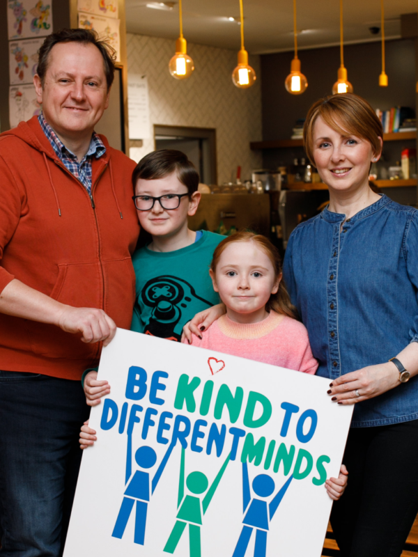 Family photographed together holding a 'be kind to different minds' poster
