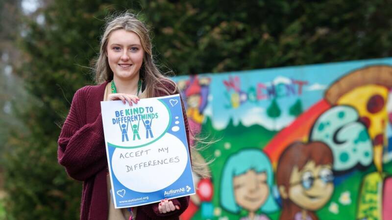 An Autism NI member posing with a 'Be kind to different minds' poster