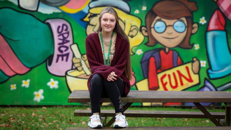 Girl sitting on a picnic bench in front of a graffiti wall