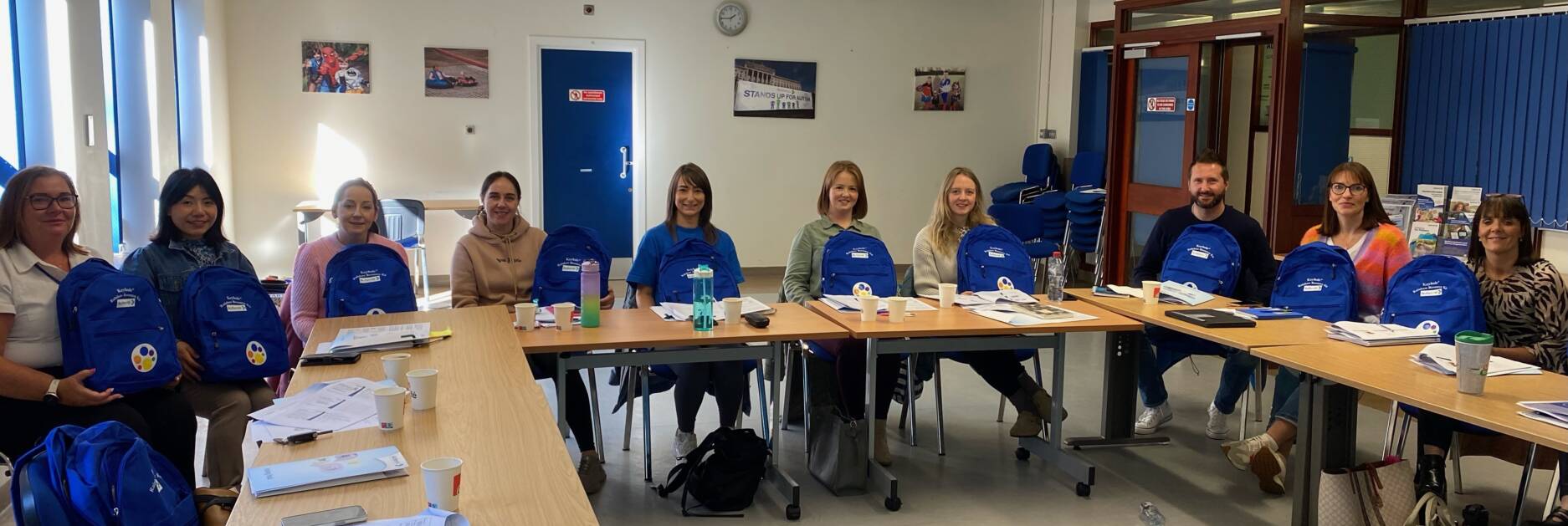 A group of people sitting in a classroom holding backpacks