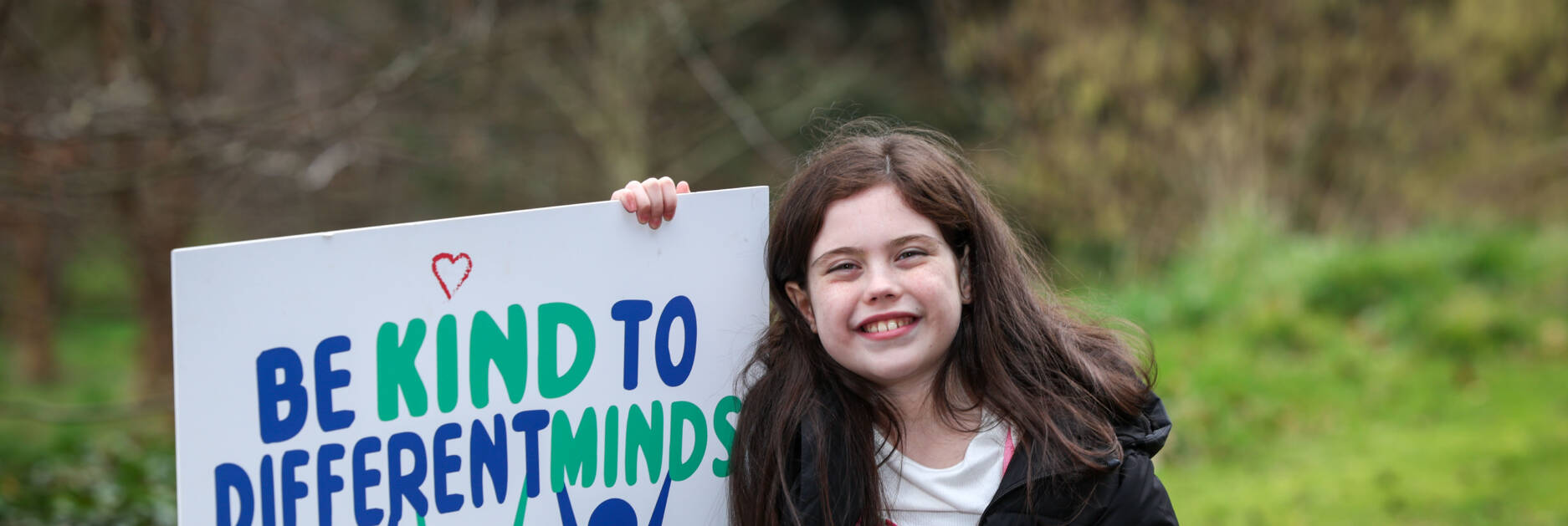 Autism NI member posing with a 'Be kind to different minds' poster